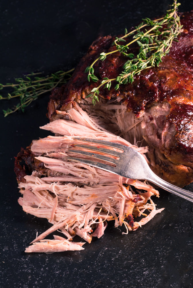 Titelbild für die Zubereitung für ein Gericht mit Pulled Pork. Hierfür liegt ein bereits halb gepulltes Fleischstück mit einer Gabel auf einer Schieferplatte.