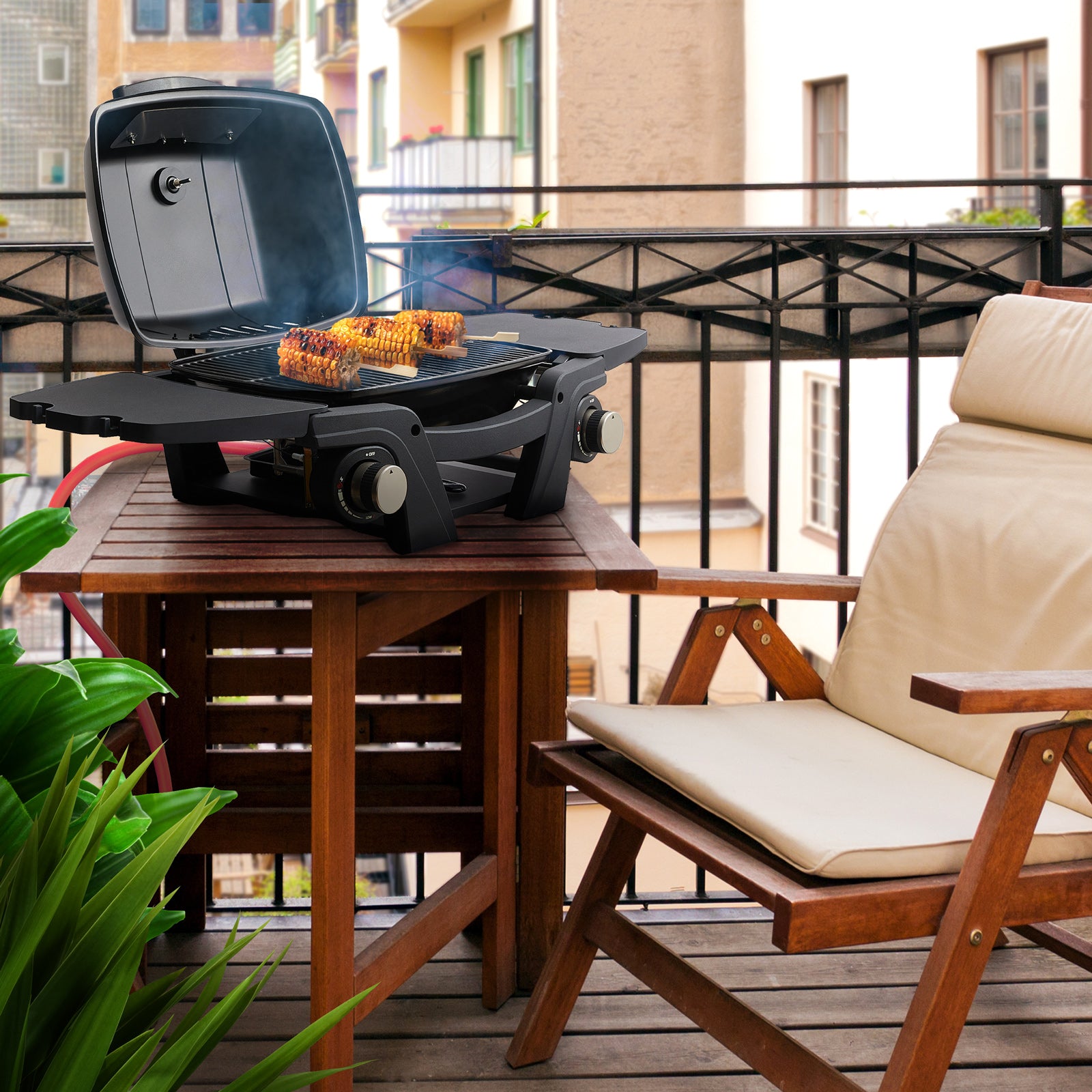 Der TAINO MAHTO Tischgrill steht mit geöffnetem Deckel und Grillgut auf dem Rost auf einem Balkon