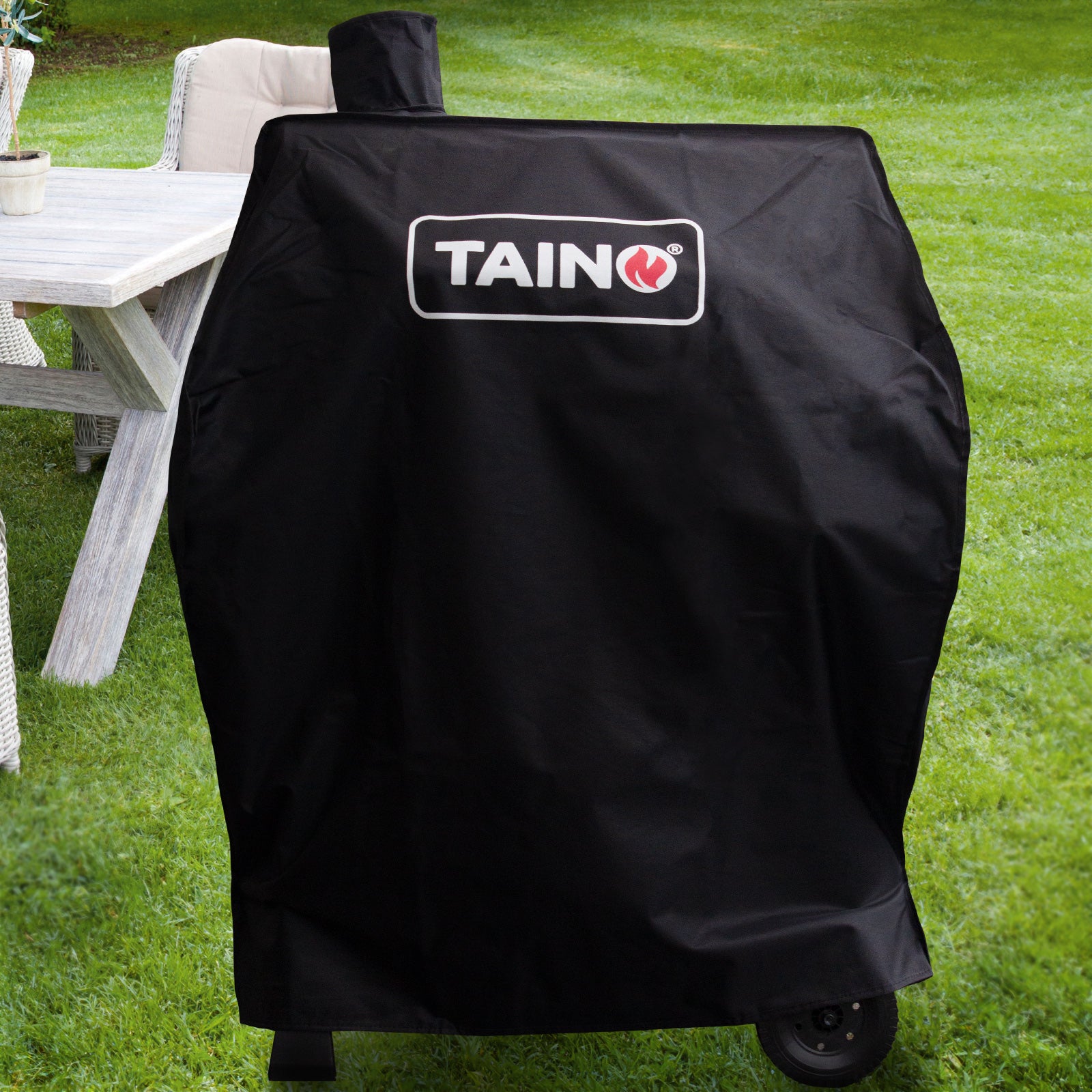 Taino Grill unter der passenden Abdeckhaube in einem Garten vor einem weißen Tisch