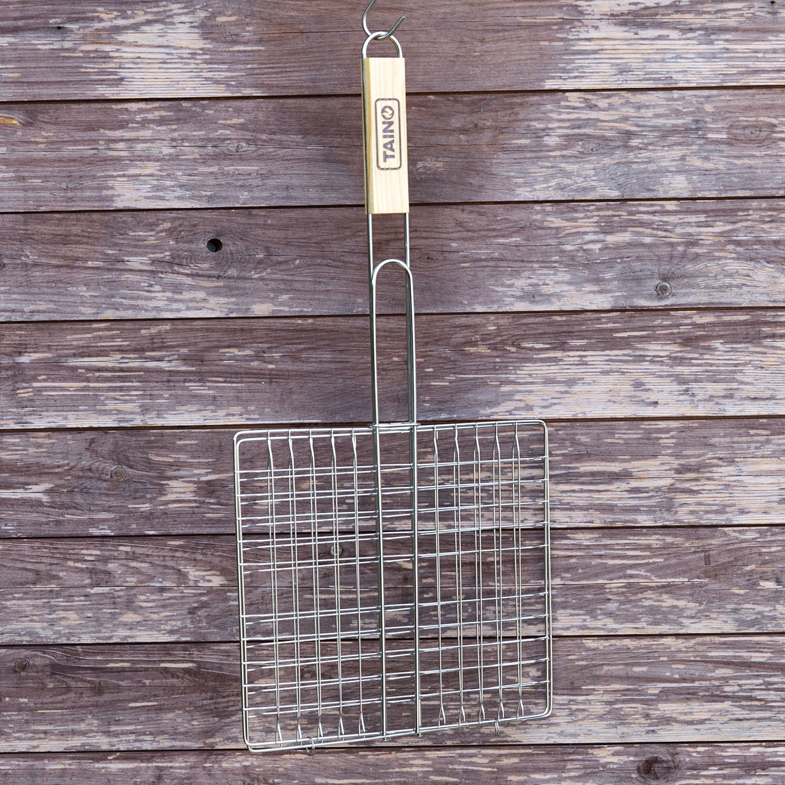 Edelstahl Grillkorb mit Holzgriff hängt an einem Haken vor einer Holzwand