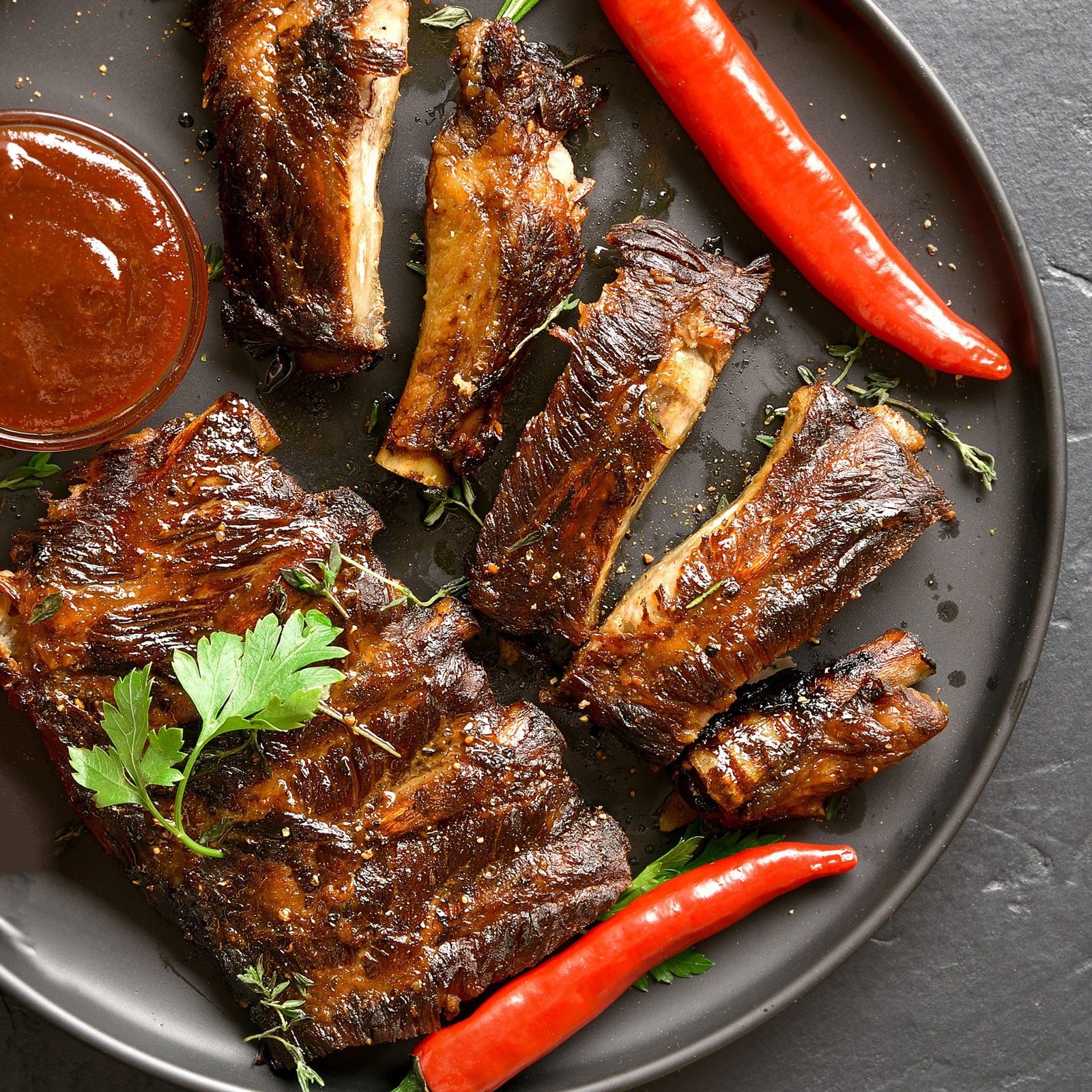 Auf einem Teller sind knusprig zarte Spareribs mit Barbecue Sauce angerichtet, verziert mit Petersilie und zwei Chilischoten