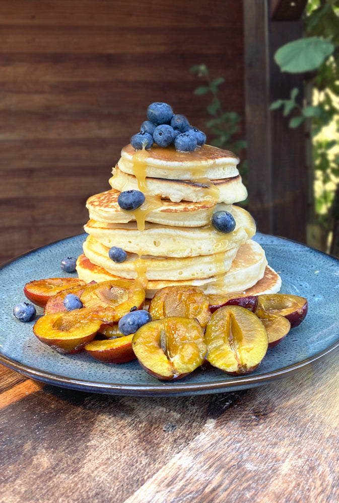 Fluffige, amerikanische Pancakes auf einem Teller angerichtet mit Pflaumen und Blaubeeren.